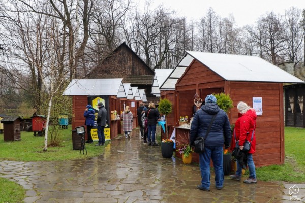 Drewniane budki - stoiska z lokalnymi produktami, przy stoiskach ludzie oglądają produkty