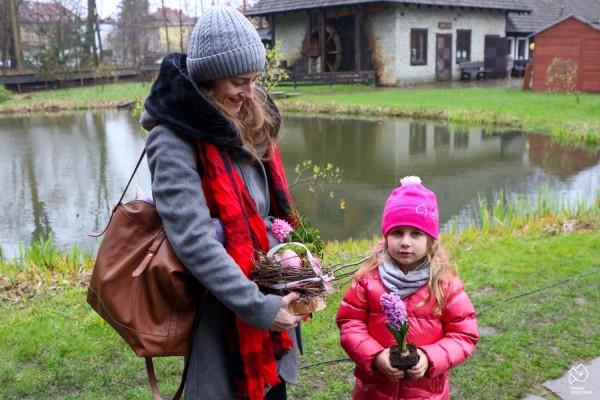 Kobieta trzymająca ozdobę wielkanocną, obok dziewczynka trzymająca kwiatek w doniczce