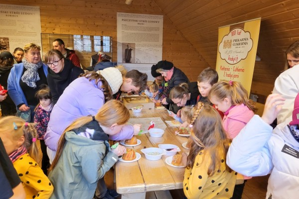 Uczestnicy warsztatów ozdabiają przy stole mini babki wielkanocne i małe mazurki