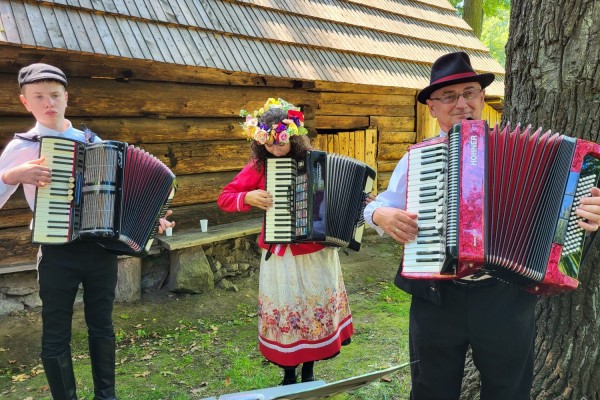 Trzy osoby w strojach regionalnych grają na akordeonach