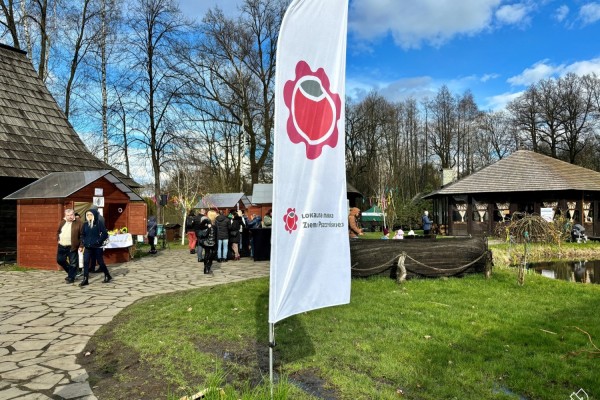 Widok na pszczyński skansen. Na pierwszym planie flaga z logo Lokalnej Marki Ziemi Pszczyńskiej.