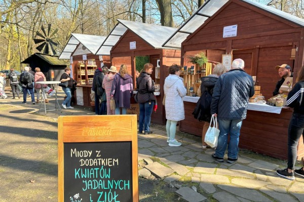 Klienci oglądają produkty na stoiskach podczas jarmarku w skansenie.