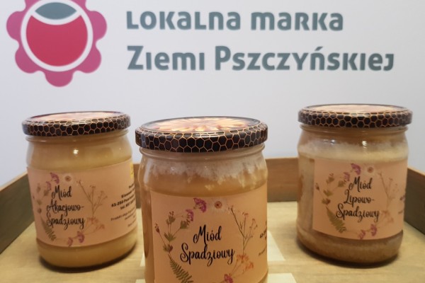 Słoiki miodu: akacjowo-spadziowego, spadziowego, lipowo-spadziowego na tacy, w tle logo Lokalnej Marki Ziemi Pszczyńskiej.