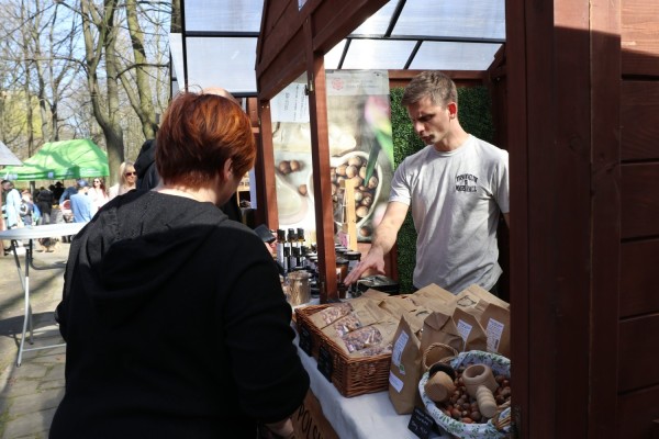 Klienci oglądają produkty na stoiskach podczas jarmarku w skansenie.