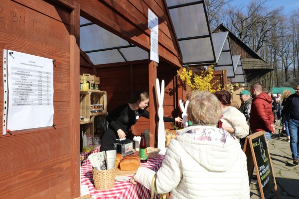 Klienci oglądają produkty na stoiskach podczas jarmarku w skansenie.