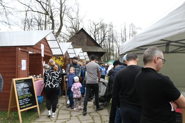 Klienci oglądają produkty na stoiskach podczas jarmarku w skansenie.