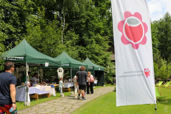 Na terenie skansenu namioty ze stoiskami lokalnych produktów, na pierwszym planie flaga z logo Lokalnej marki Ziemi Pszczyńskiej.